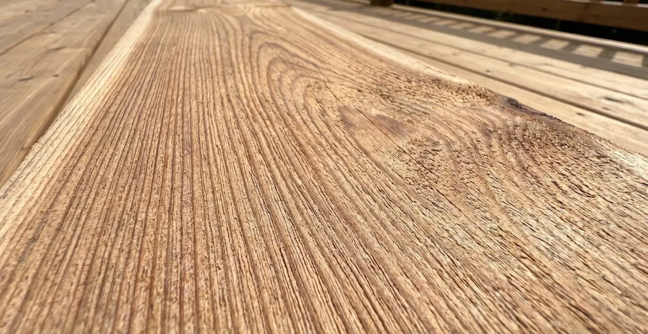 Plan rapproché sur la texture d'une lame de terrasse en bois montrant le grain et les nervures naturelles avec un jardin flouté en arrière-plan